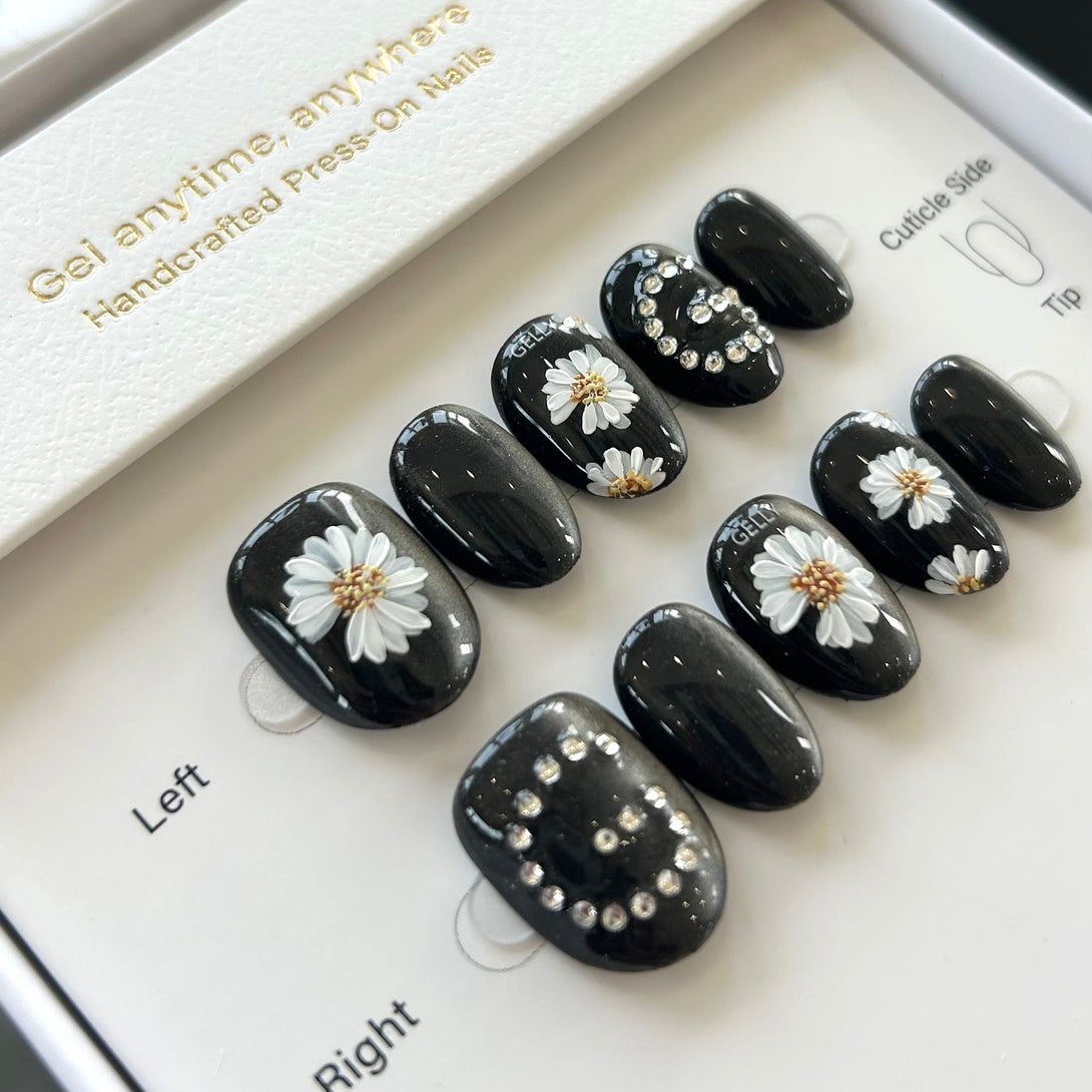 Black press-on nails with white daisy flowers and rhinestones on a display card.