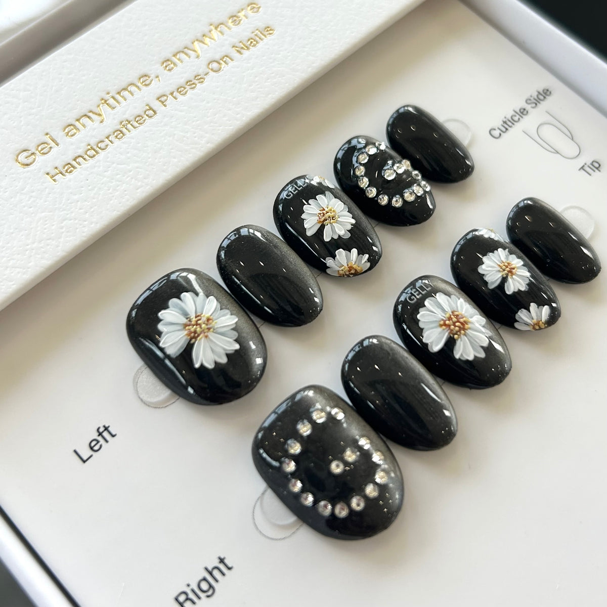 Black press-on nails with white daisy flowers and rhinestones on a display card.