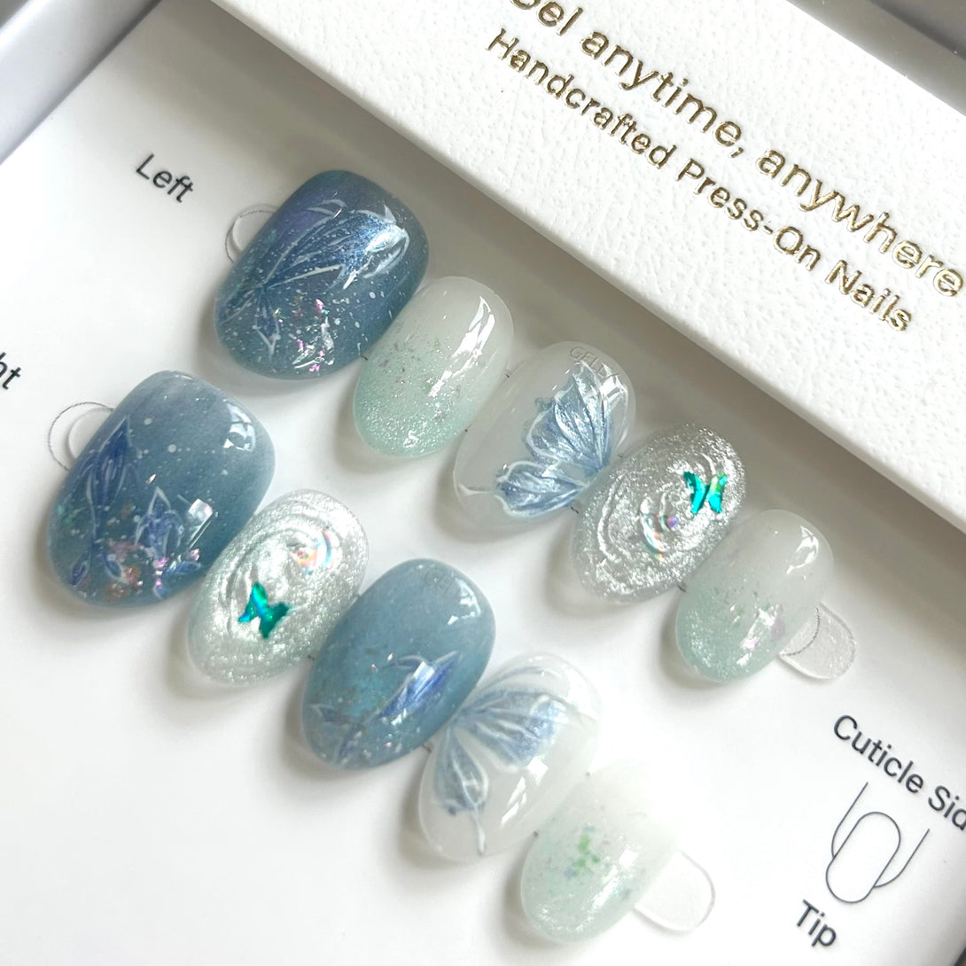 Set of blue and white press-on nails with butterfly designs in a box.