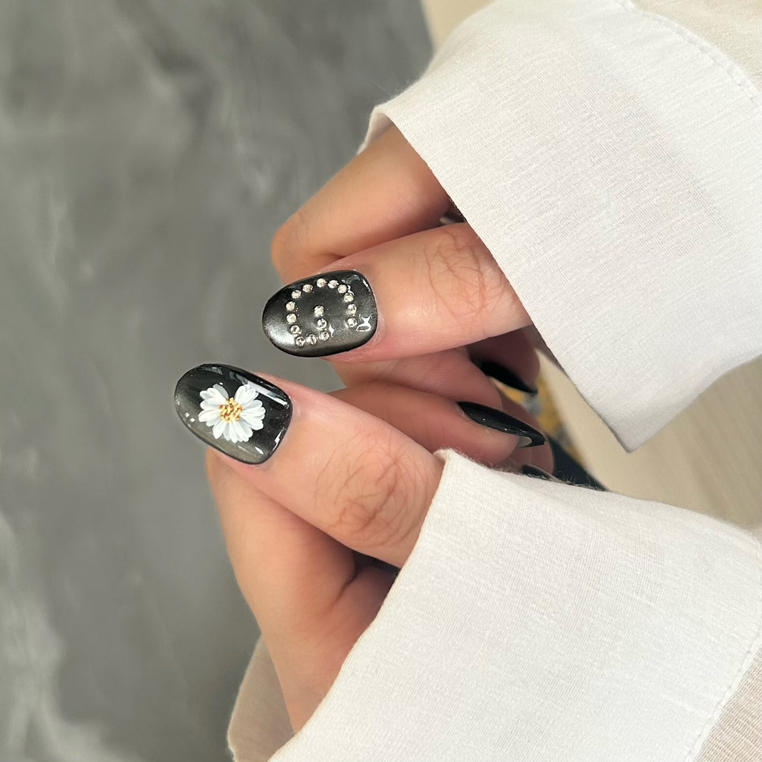 Close-up of a hand with black nail polish featuring floral designs.