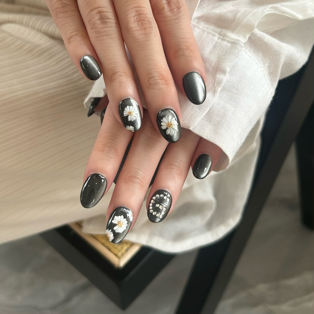 Hand with black nail polish and floral designs on a neutral background
