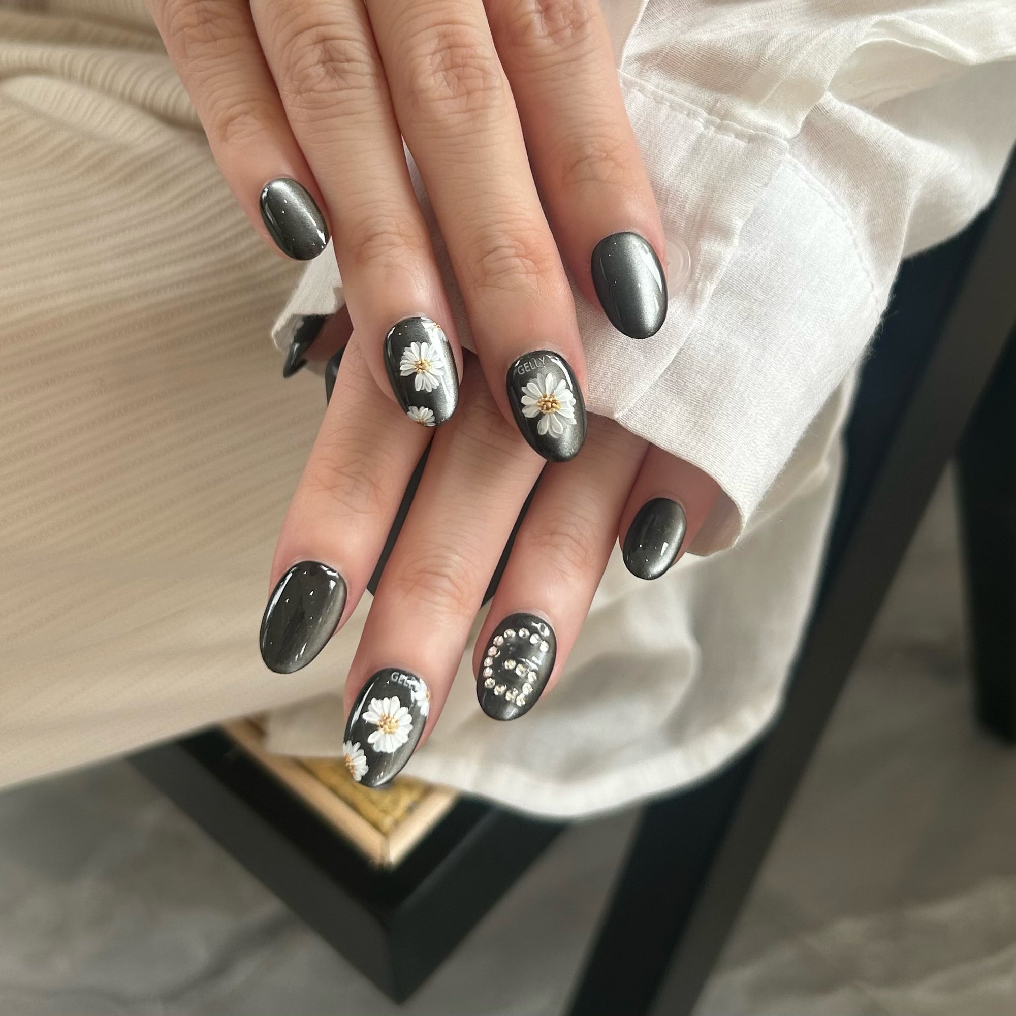 Hand with black nail polish and floral designs on a neutral background